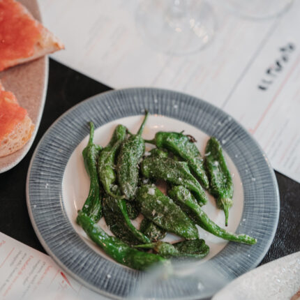 A plate of blistered Padrón peppers alongside pan con tomate.