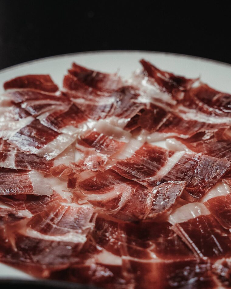 Thinly sliced Jamón Ibérico served on a wooden board with picos.