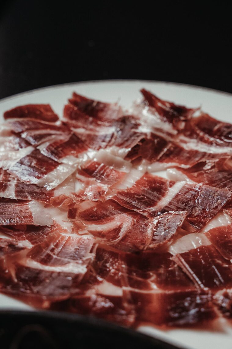 Thinly sliced Jamón Ibérico served on a wooden board with picos.