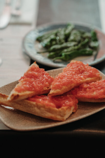 A plate of blistered Padrón peppers alongside pan con tomate.