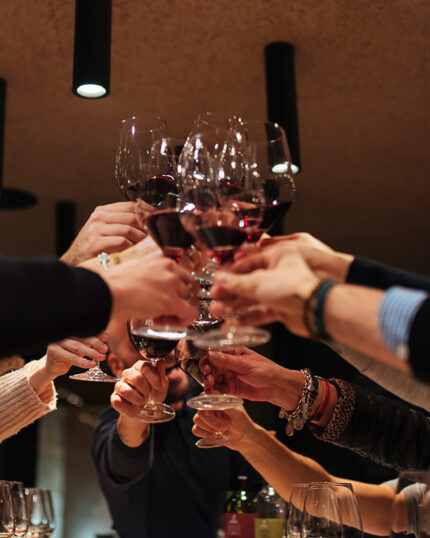 A large group of people clinking glasses of red wine together in a celebratory toast under modern lighting.
